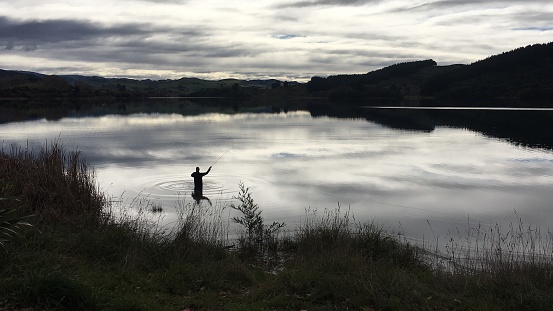 A man engaged in the peaceful activity of fishing in a remote mountain lake, surrounded by breathtaking landscapes. Perfect for themes of tranquility, for themes of nature, wilderness, outdoor activities, escape, and relaxation.