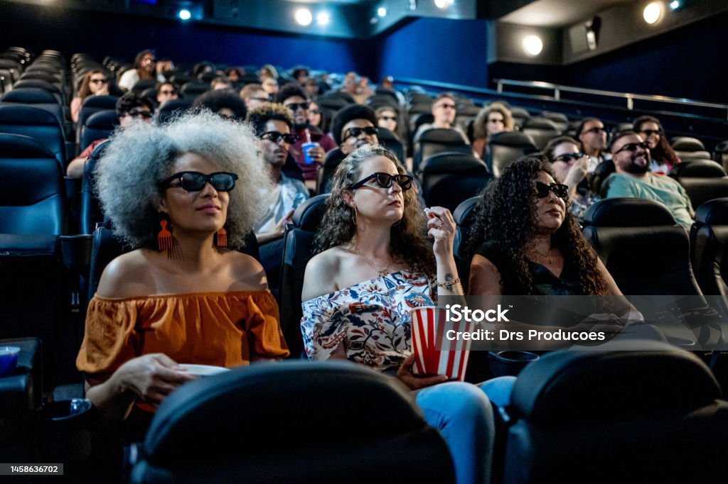 Mature female friends watching 3D movie at cinema Movie Theater Stock Photo