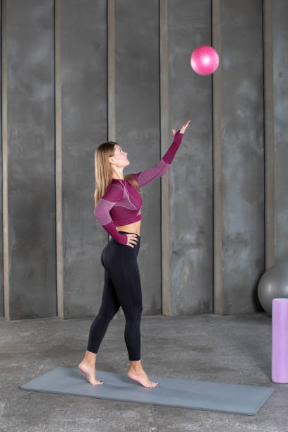 istock A Pilates and gymnastics instructor throws a pink ball while standing on a yoga mat. 1458641221