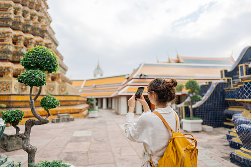 Young  Caucasian woman photographing with  smartphone in Wat Pho temple in Bangkok