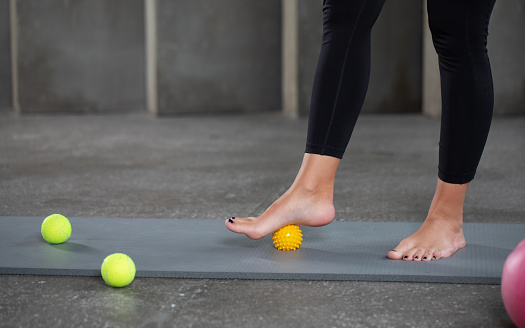 A woman does self-massage of the feet with a prickly ball, myofascial release, relaxation of the muscles of the foot. MFR.