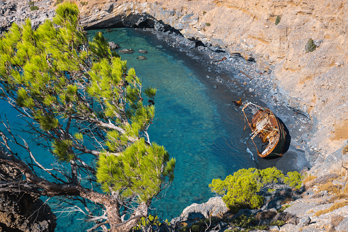 Shipwreck on idyllic beach near Agios Ioannis, South Crete. View from above through the green pine trees.
