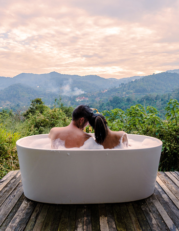 A couple of caucasian men and Asian women in a bathtub in the evening during sunset, a couple in a bathtub.