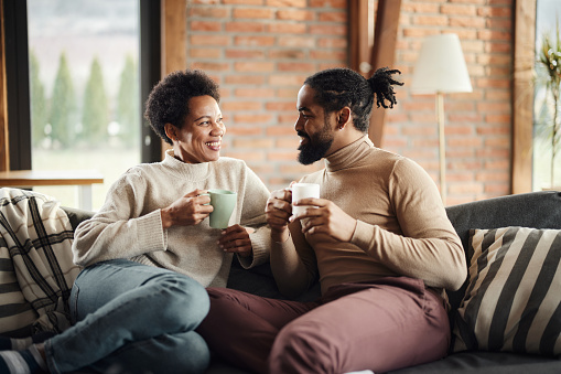 Happy African American couple communicating while drinking coffee on sofa in the living room.