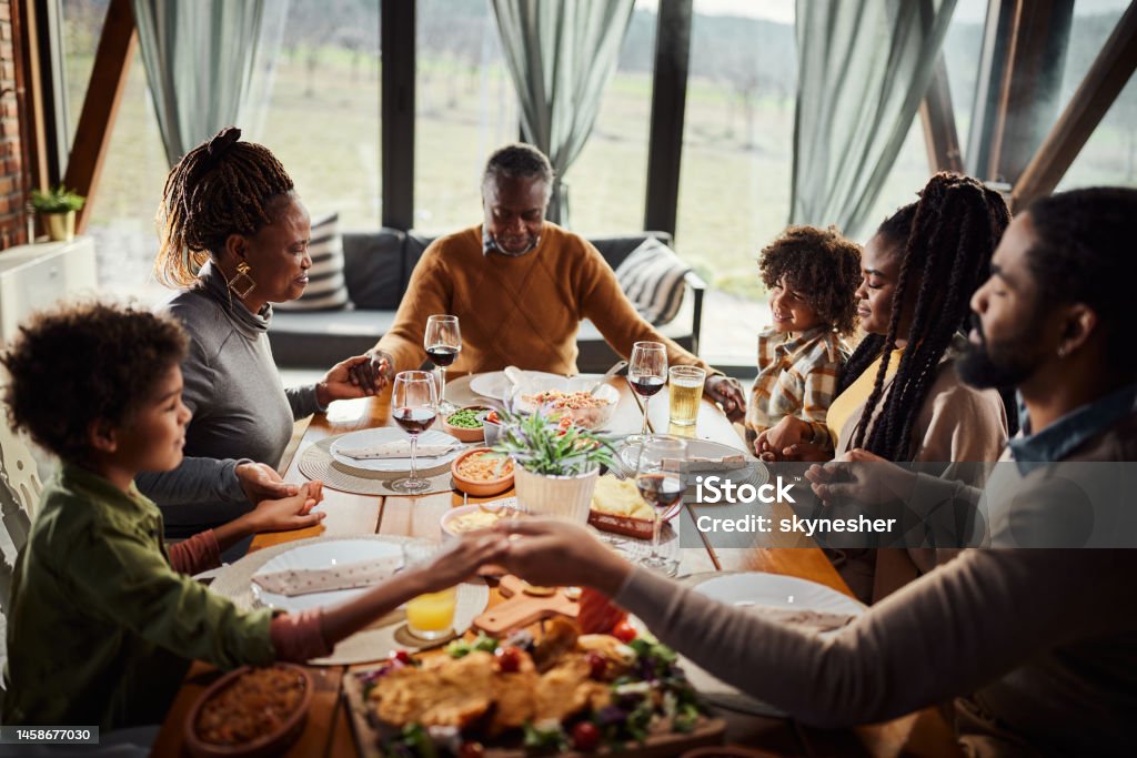 Praying before a meal! Religion African American extended family holding hands while praying before lunch at dining table. Praying Stock Photo