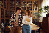 Happy high school couple talking in library.