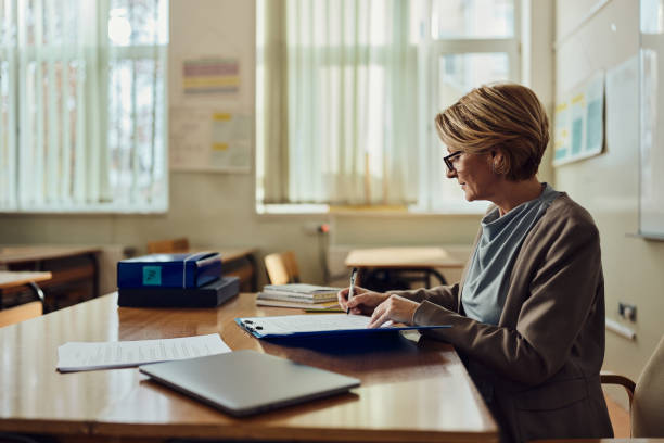 insegnante donna che scrive i suoi piani in classe. - solo una donna matura foto e immagini stock