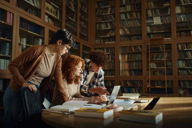 groupe de lycéens utilisant un ordinateur portable dans la bibliothèque. - teenager adolescence campus group of people photos et images de collection