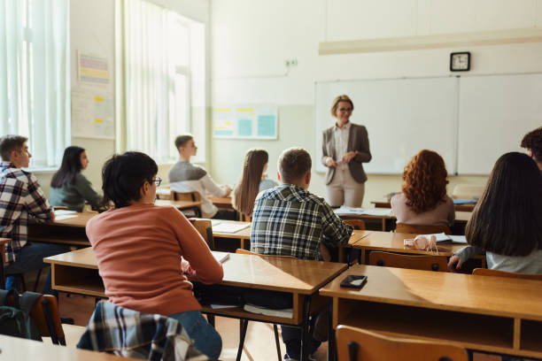 back view of high school students listening to their teach on a class. - klaslokaal fotos stockfoto's en -beelden