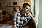 Thoughtful male students looking through window on a break in the classroom.