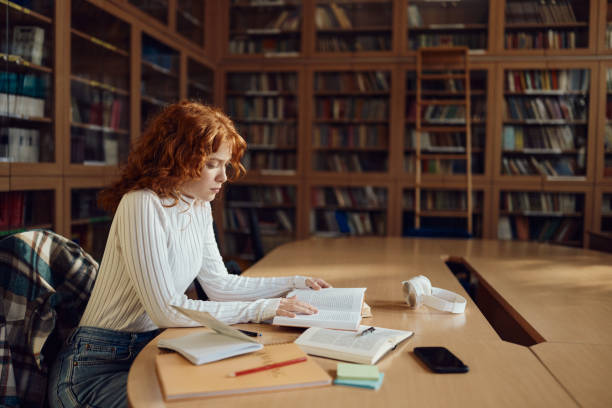 Redhead female student reading a book in library.