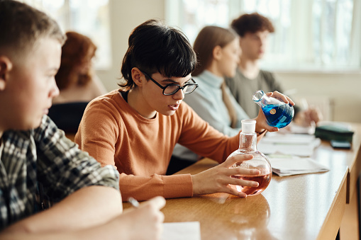 Female high school student mixing chemicals while having a science class with her friends in the classroom.