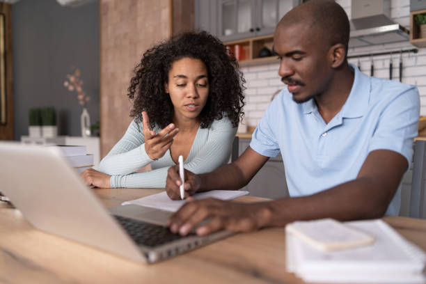 istock Modern young African American couple watching online learning classes, sitting in the kitchen, taking    notes and discussing, e-learning concept 1458681187