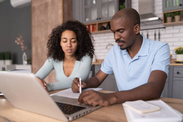 istock Modern young African American couple watching online learning classes, sitting in the kitchen, taking    notes and discussing, e-learning concept 1458681194