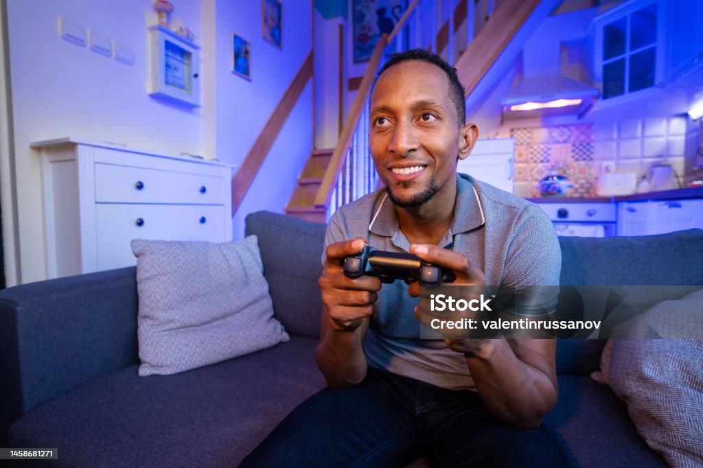 Smiling  brazilian young man enjoying videogame on playstation, having fun at home. Happy brazilian young man enjoying videogame on playstation, having fun at home. 25-29 Years Stock Photo