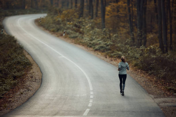 rückansicht einer sportlerin, die auf der straße in der natur joggt. - road running stock-fotos und bilder