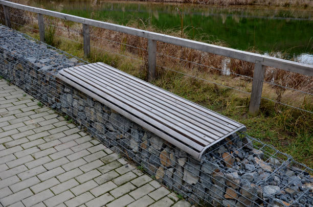 lac de baignade zone côtière aménagée d’eau peu profonde et une partie plus profonde pour la baignade. clôturé avec poutres en bois clôture et mur de gabions avec bancs de planches. bassin de rétention, réservoir, source, feu, sec - retention pond photos et images de collection