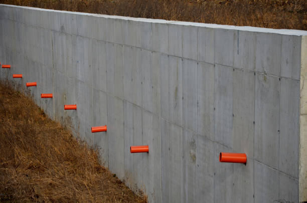 long straight supporting wall of cast cement mixer formwork. behind wall is soil that is brought out through the wall by drainage pipes. sewer pipe drain in line. construction site, white, field, armature, grouting, concreting, hardening, infrastructure, reinforcing, monolithic, soil, soil, stabilizer, timbering