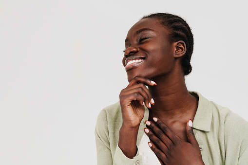 Young beautiful happy smiling african woman with braided hair and closed eyes touching her chest and chin while standing over white isolated background