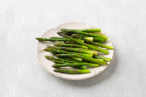 Steamed asparagus on a plate on a light gray background, top view. Healthy diet food