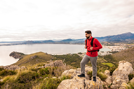 Hiker standing in front of the landscape on the north coast of Mallorca with the bay of Pollensa in the background. Color editing. Part of a series.