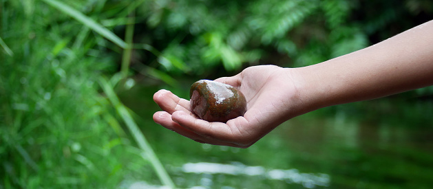 A woman's hand holding a zen basalt stone which she got from deep in the clear river water