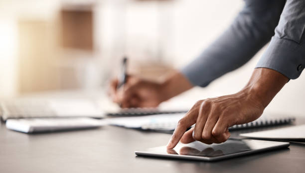 istock Businessman hands, tablet and writing notes, planning agenda or analytics at office desk. Closeup writing notebook, digital ideas and online website, internet and economy research of finance manager 1458699172