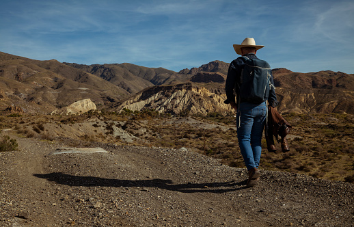 Rear view of adult man in cowboy hat walking on dirt road in desert. Almeria, Spain