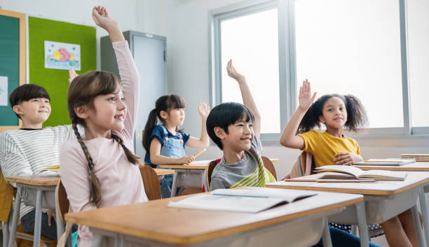istock Pupil boy active learn with teacher in classroom at elementary school. Student boy girl studying in primary school. Many hands of volunteers during class room raise hand answer question banner 1458700630