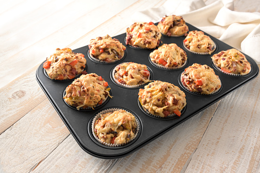 Pizza muffins in a baking tray fresh from the oven, made from yeast dough with vegetables, sausage and cheese, finger food as a party snack, selected focus, narrow depth of field