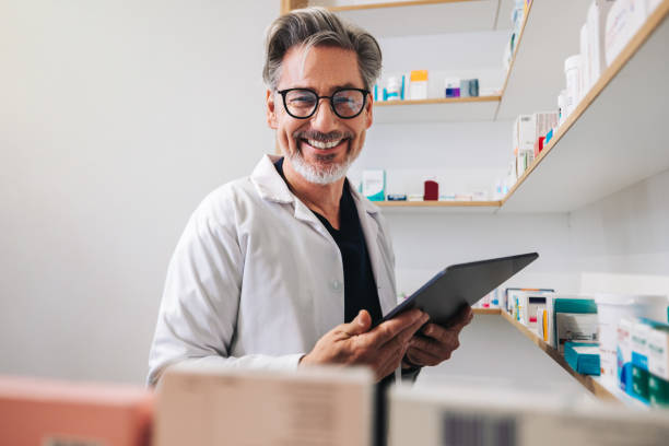 farmacéutico feliz sosteniendo una tableta en una farmacia - pharmacist mature adult smiling senior adult fotografías e imágenes de stock