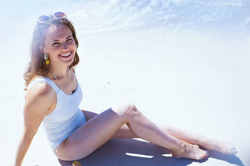 happy modern 40 years old woman in white beachwear sitting at the beach.
