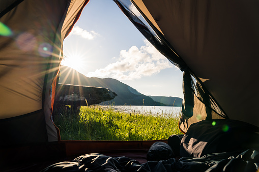 View from the inside of a tent in beautiful mountain and water landscape with sun over the mountains