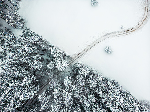 Aerial view of a snow covered country road going hrough the white snow winter forest. Top drone view.