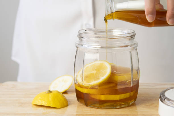 istock woman's hand pouring honey in a clear jar with lemon 1458708356