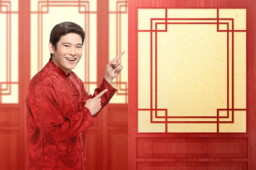 An Asian Chinese man in a cheongsam dress pointing to something. Happy Chinese New Year