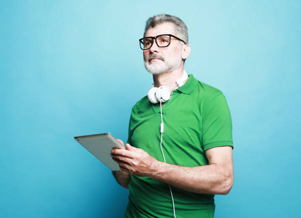 istock Happy senior bearded man wearing eyeglasses and headphones using digital tablet. 1458709432
