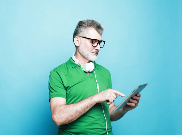 istock Happy senior bearded man wearing eyeglasses and headphones using digital tablet. 1458709436