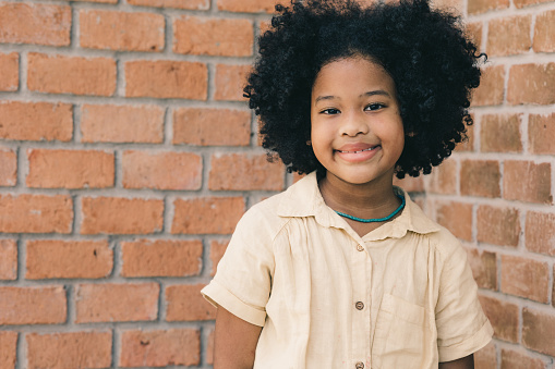 cute black African healthy child girl standing happy smile with copy space brick wall in school.