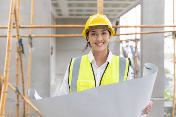 istock happy woman architect home builder project manager work in construction site with blueprint floor plan looking camera smiling 1458711243