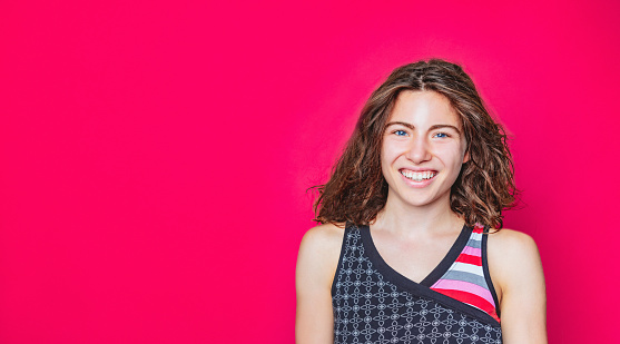 Portrait of serene young woman with blue eyes and wavy brown hair smiling at camera on vivid magenta background