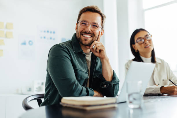 Business man listening to a discussion during a meeting Business man listening to a discussion during a meeting in an office. Happy business man sitting in a boardroom with his colleagues. real life stock pictures, royalty-free photos & images