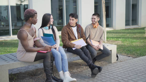 Four students sitting on the university campus. Multi-ethnic group of students with folders in hand stock photo