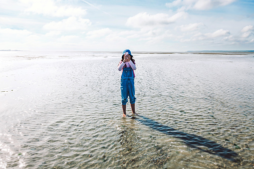 girl taking mobile picture and standing in low tide sea water in le crotoy, france