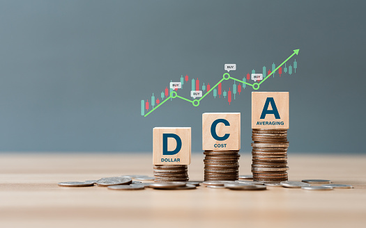 DCA word on a wooden cube on coins in idea Dollar Cost Averaging investment strategy, Saving stock or savings on a monthly, quarterly basis.