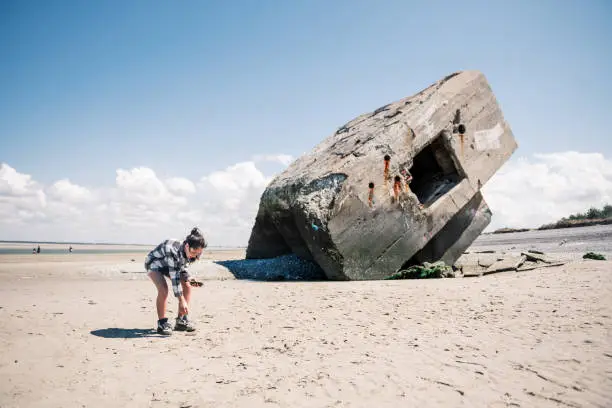 Photo of girl crouching in the sand  infront of old  german concrete  bunker at french beach