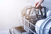 Hand holding cutlery basket with clean cutlery in open dishwasher in kitchen