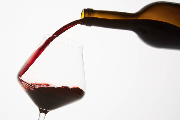 istock Red wine pouring into tilted wineglass from bottle. 1458726634
