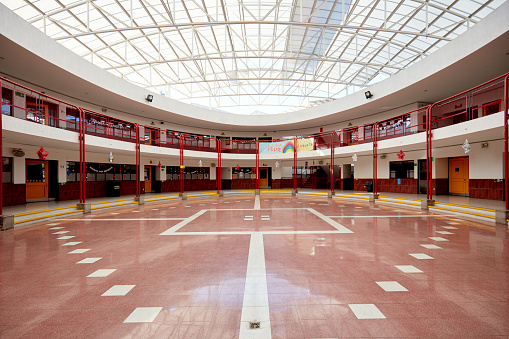 Wide angle view of school building interior, windows to classrooms, polished floor with markings for sports activity, and glass ceiling.