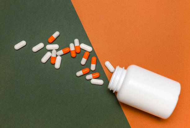 istock white bottle and scattered pills on a green-orange background 1458736309